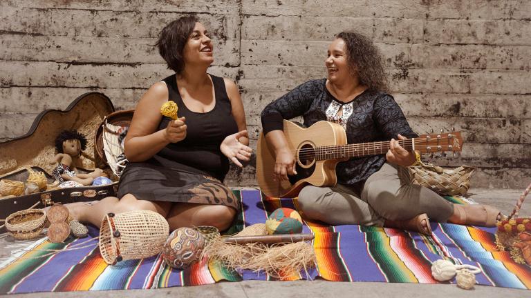 ladies sat down on a rug playing guitar